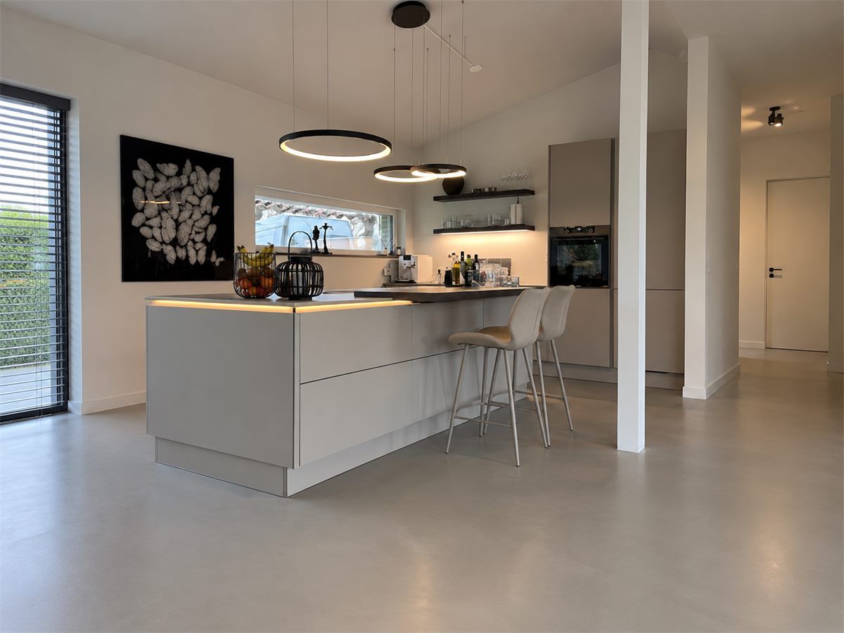 Gietvloer in een moderne keuken in Oosterhout Grijze gietvloer in een moderne keuken met kookeiland en barkrukken in Oosterhout